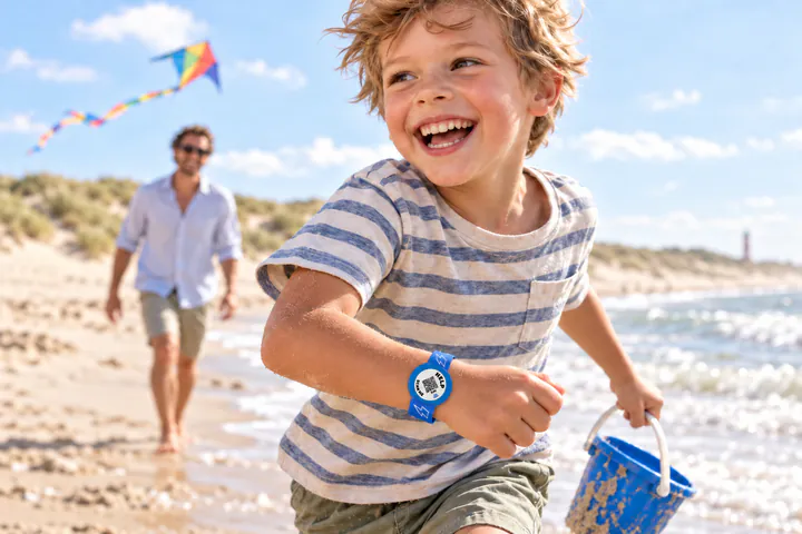Lachende jongen op het strand met de blauwe ICESCAN-kinderarmband om zijn pols (AI-beeld)