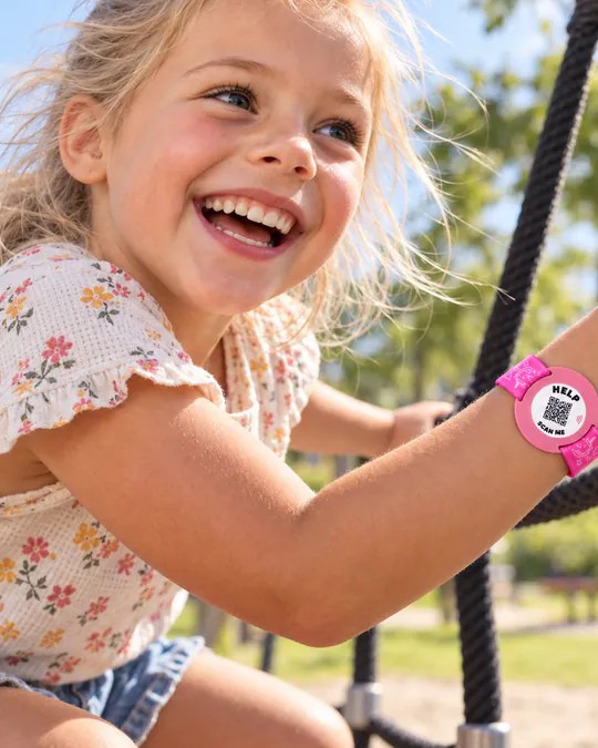 Een lachend meisje speelt in een zonnige speeltuin, met een roze ICESCAN-armband om haar pols.